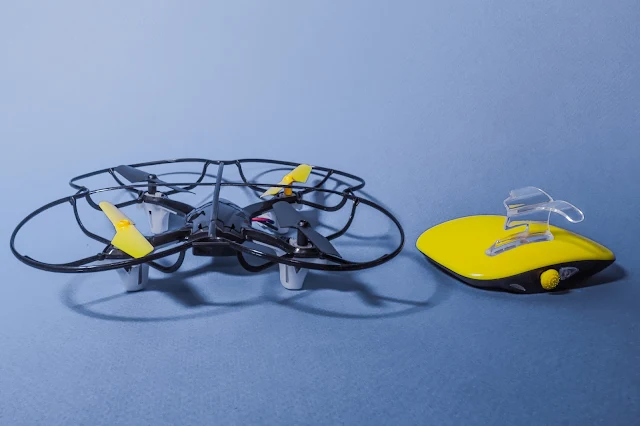 A small quad helicopter drone and a yellow and black motion controller to hold in your hand.