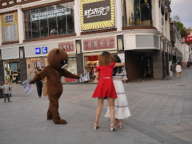 young woman hiding behind her friend from a person in a bear suit