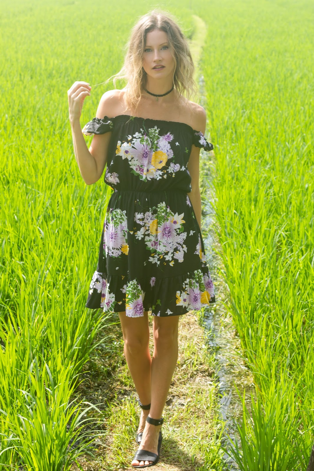 fashion and travel blogger, Alison Hutchinson, i s wearing the KAYVALYA Rosie Off The Shoulder Dress in Black Floral in a rice field in Bali
