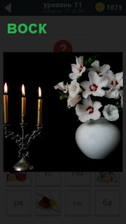 В канделябре стоят восковые горящие свечи и ваза с цветами на темном фоне