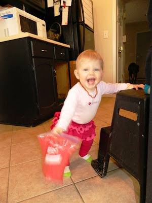 Young tot standing on kitchen tile floor holding a bag of red rice