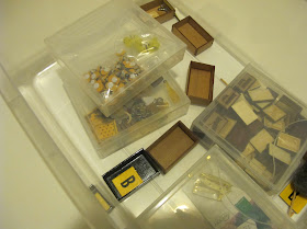 Plastic tub containing a number of miniature wooden crates and packages of miniature items.