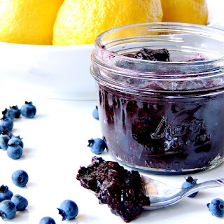 Quick and easy, and uber tasty, this Blueberry Chia Jam recipe is not just awesome because of its flavor, it is wonderful because it packs some healthy super food punch! #blueberry #jam #chia #healthy #glutenfree #vegan #easy #recipe | bobbiskozykitchen.com Blueberry Chia Jam in a glass jar with a silver spoon on a white background with lemons and blueberries around it.