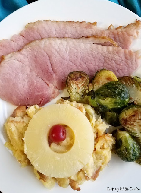 Scalloped pineapple is a perfect slightly sweet side dish to go along with a salty ham dinner. It will feel right at home on your holiday plate! dinner plate with scalloped pineapple, brussels sprouts and slices of ham