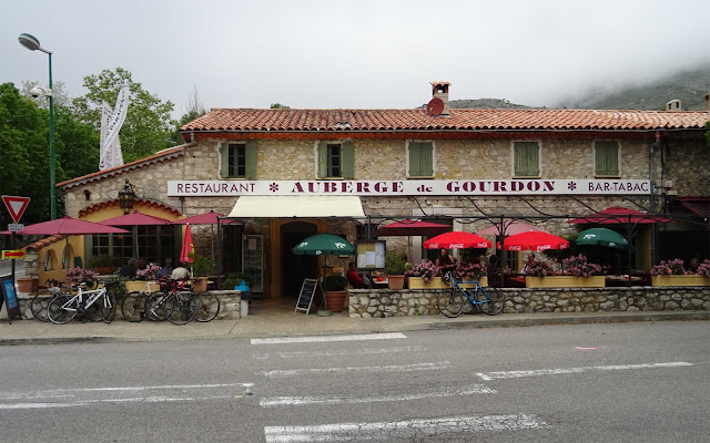 Restaurant Auberge gegenüber dem Parkplatz mit grünen Fensterläden und rotem Dach in Gourdon