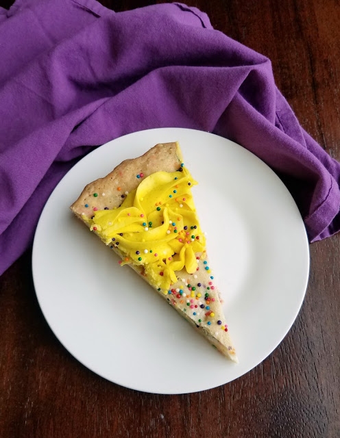 A supersized chewy vanilla cookie filled with plenty of festive sprinkles and white chocolate chips and topped with frosting and more sprinkles. This cookie cake is what birthday dreams are made of.