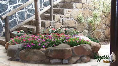 Canteiro com pedras do rio com as paredes de pedra, a escada de pedra e o corrimão de madeira.