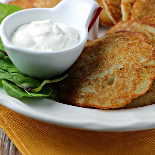 Easy Potato Pancakes by Renee's Kitchen Adventures on a white plate with a lettuce garnish and sour cream