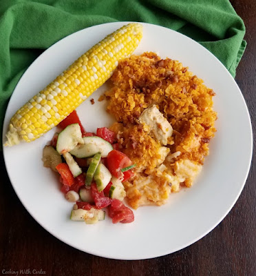 Cheesy potatoes with a ranch twist and topped with buffalo chicken, bacon, more cheese and plenty of buttery corn flakes. What's not to love? dinner plate with buffalo chicken casserole, cucumber salad and corn on the cob