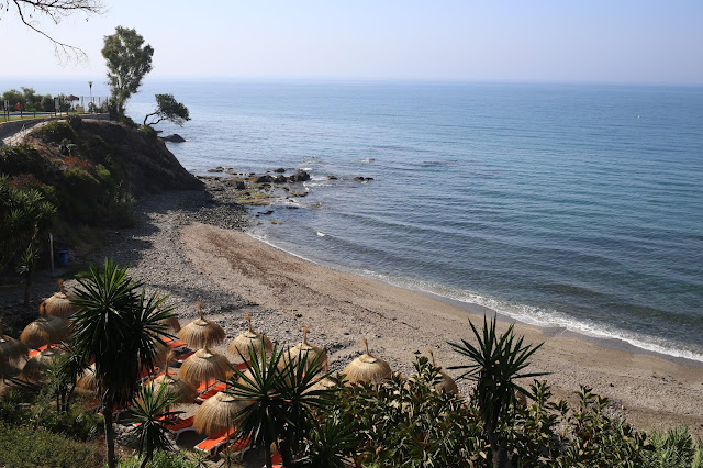 Playa con sombrillas de paja y acantilados con vegetación a su espalda.