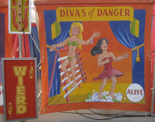 Divas of Danger painted sign with two women walking on swords and broken glass