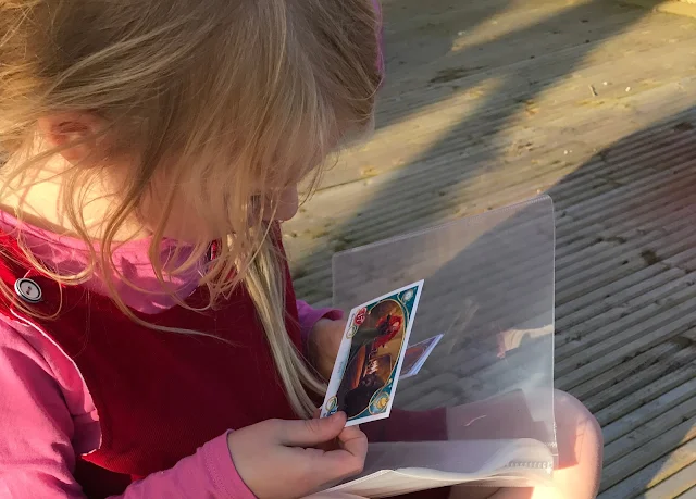 A young blonde girl sitting on decking looking at a Topps Disney Princess Trading card from Brave while holding a clear binder
