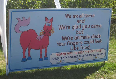 Hand-painted sign with horse cartoon and the following text: We are all tame/and/We're glad you came/but/We're animals, dude/Your fingers could look/Like food