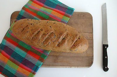 A loaf of scallion chive bread with garlic and rosemary on a wooden cutting board.