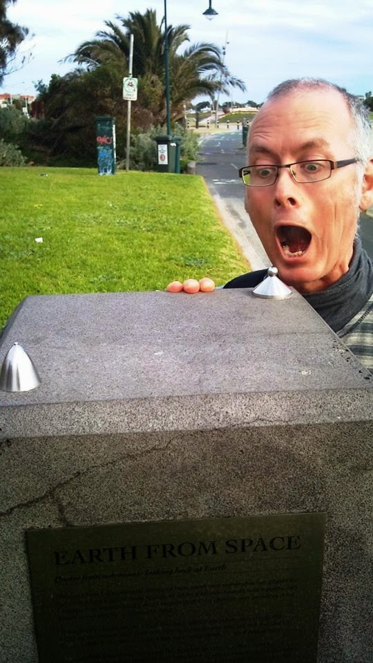 Man pretending to eat a scale model of the earth, on a plinth in a park.