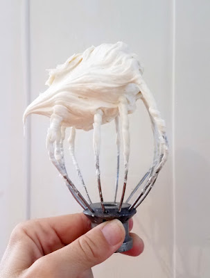 mixer whisk held upside down with a swirl of white whipped sweetened condensed milk frosting