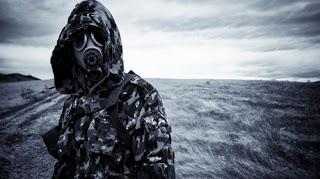 Persona con capucha y máscara de gas en un páramo.