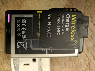 The Note 3 Charger Receiving Coil Card Taped to Battery that is in the External Charger The Note 3 wireless charging receiver coil card taped to the back of the Note 3 extra battery, which is being charged by the external battery charger, plugged into an electrical socket.