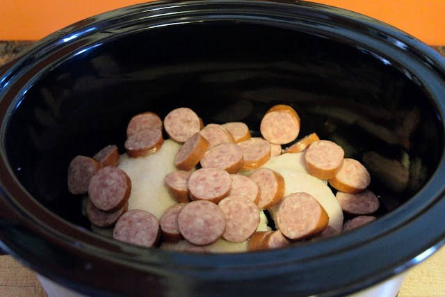 Sliced smoke sausage being added to the crockpot with the chicken.
