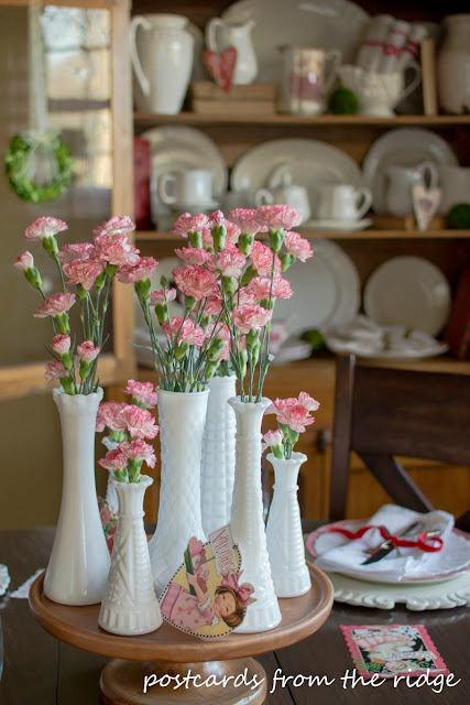 Vintage milk glass vases with carnations make a simple, pretty centerpiece. Postcards from the Ridge.