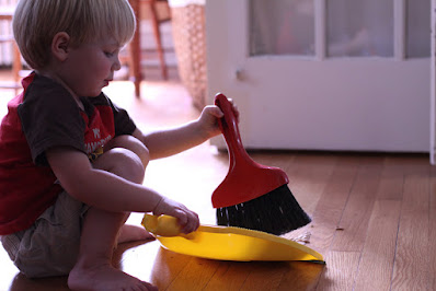 Photo of young boy squatting and holding a push broom and dustpan