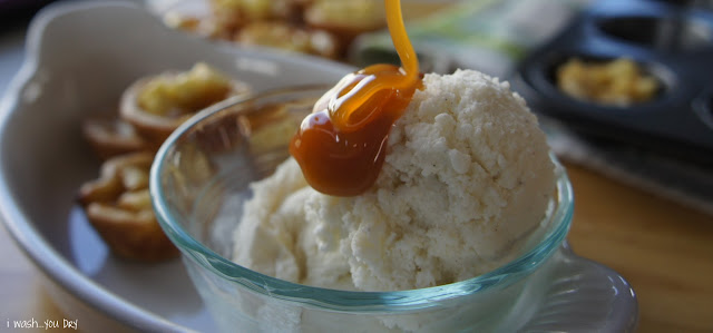A close up of Caramel sauce being drizzled on top of a scoop of ice cream in a bowl next to min apple pies. 