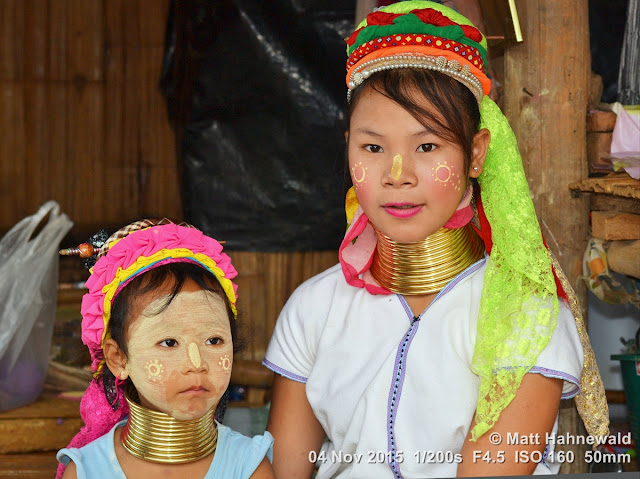 Close-up street double-portrait (groupshot) of a posing Karen long-neck saleswoman-turned-model and her younger sister, both wearing their traditional brass neck coils, Chiang Rai, Northern Thailand.