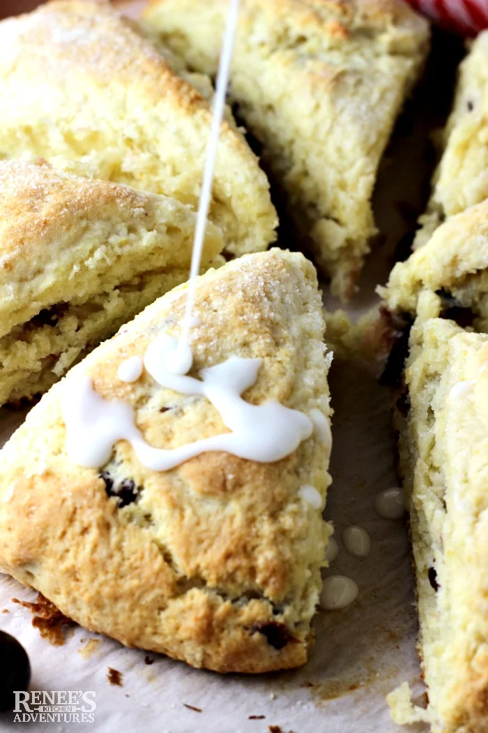 Easy Orange Cranberry Scones by Renee's Kitchen Adventures on a board with glaze being drizzled over the top of a scone