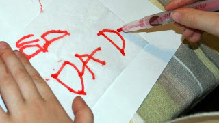 A child writing "Dad" on a piece of paper to design their own candle