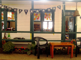 Miniature dolls' house school with bunting reading 'blogiversary' tied to the front verandah.