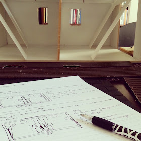 Notebook and pen on a table in front of a half-built one-twelfth scale miniature bach.