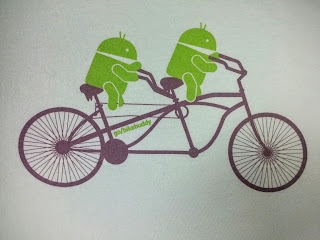 Two green Android figures atop a fanciful tandem, t-shirt design.