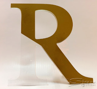 Photograph of clear acrylic flat cut acrylic letter with gold vinyl applied to create a gold looking letter.