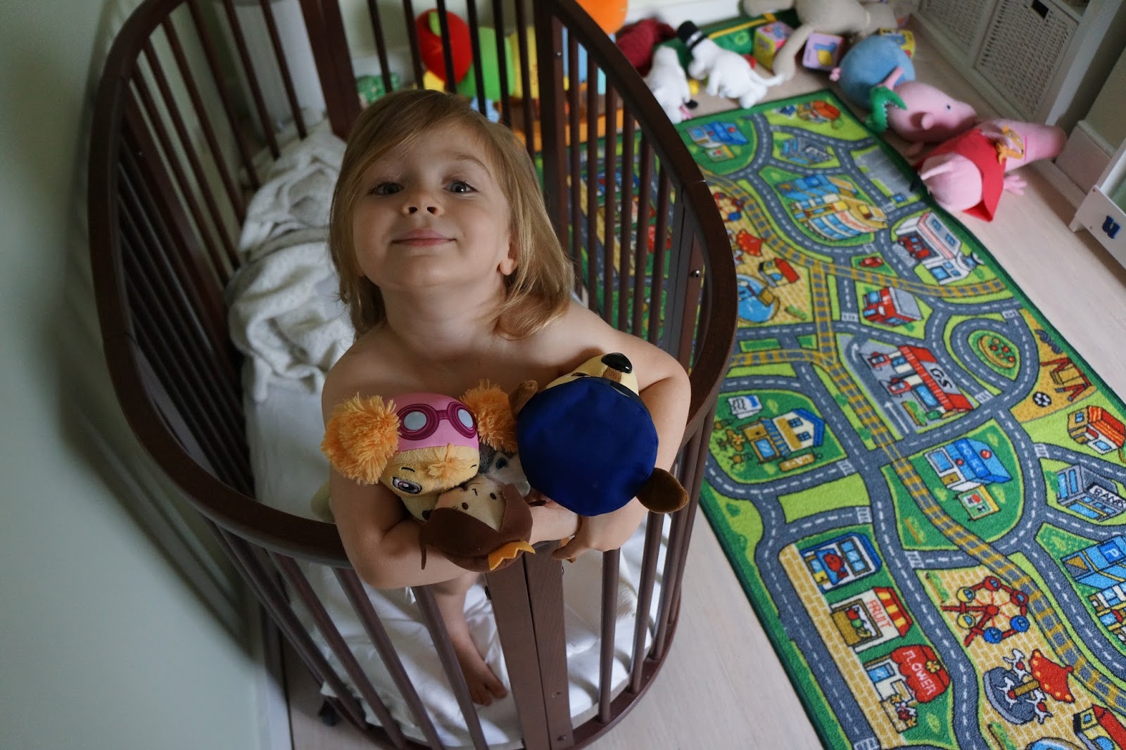 how my kid tries to avoid sleeping - girl standing in bed holding her teddies