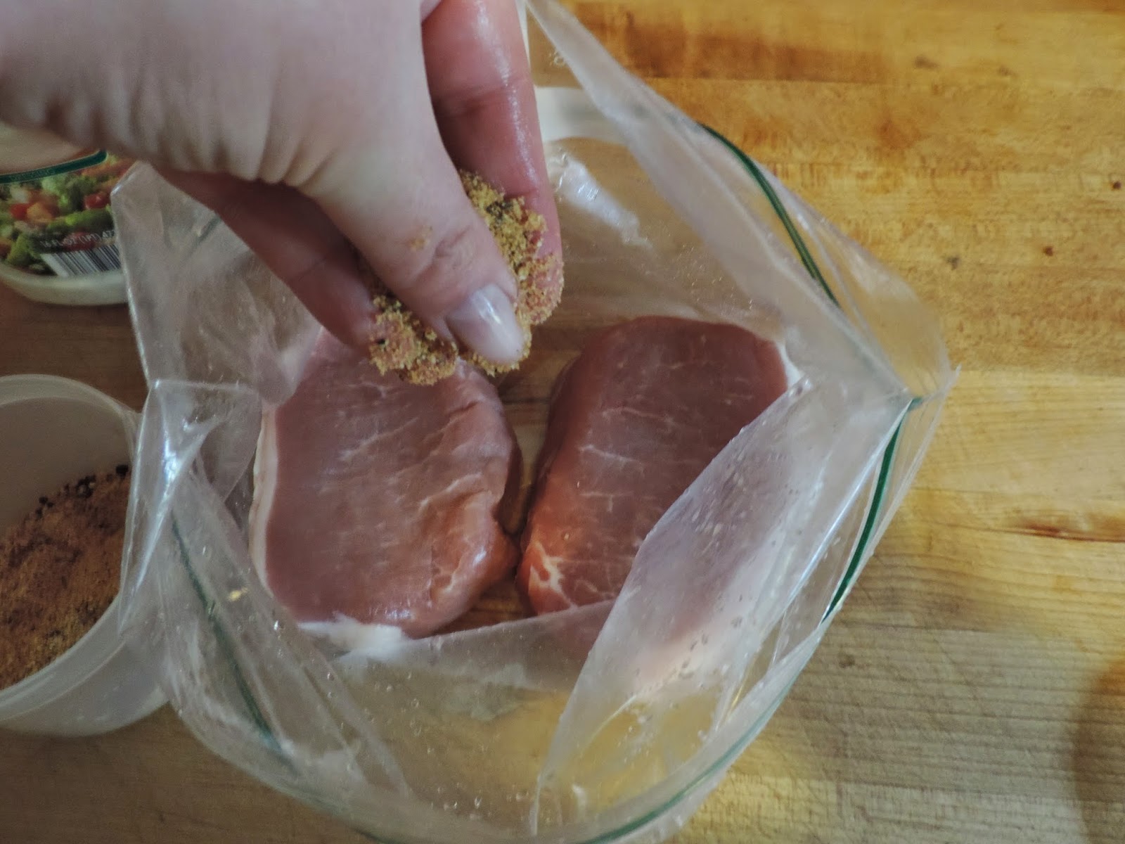 The pork chops in a resealable bag, being seasoned with an all purpose seasoning.  