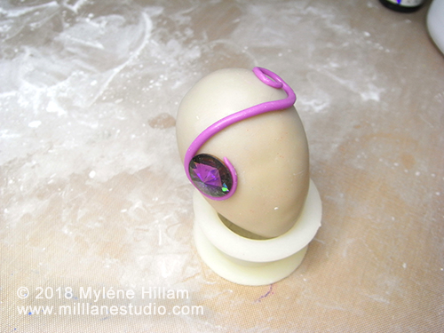 Epoxy resin clay coiled in a "S" shape around a Swarovski crystal on a clay covered egg