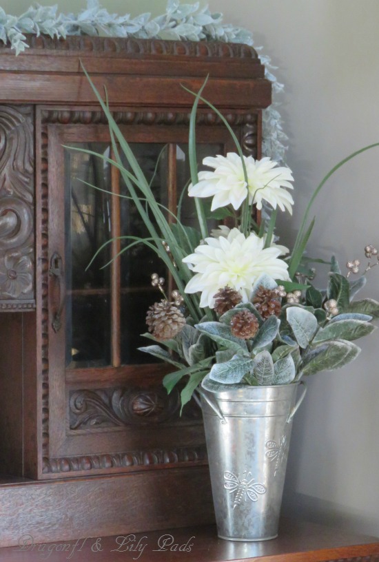 Flowers adjusted from summer to winter with greens, pine cones and gold glimmer to bring winter into this flower vase.