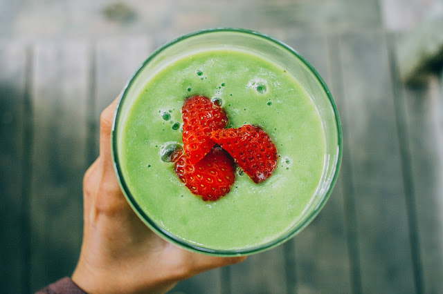 Batido de aguacate y canela mano que sujeta un vaso con batido verde de aguacate o palta y una fresa entera