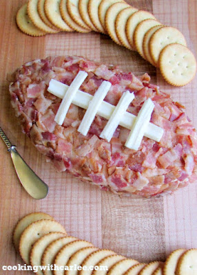 This cheese ball is sure to score with your family and friends. Bacon, cheddar and ranch come together in this football shaped treat. Perfect for the big game or any get together! pig skin cheese ball on maple cutting board with crackers nearby