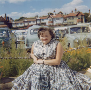 colour picture of my mum sitting on a wall wearing a flowing colourful dress.