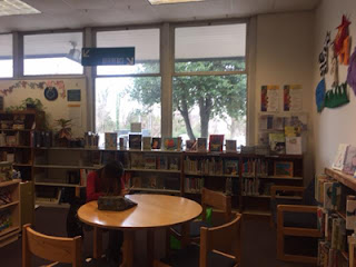 Children's Area girl sitting at a table reading a book with brightly decorated walls behind