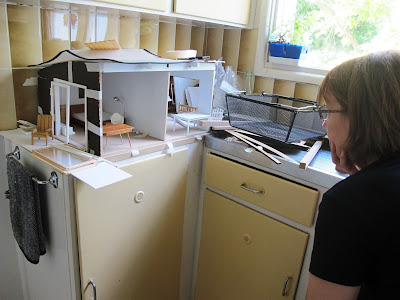 Woman looking at a dry-fitted modern miniature doll's house shed on a kitchen bench.