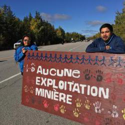 Photo : sur le bord d'une route, deux personnes autochtones, une femme et un homme, tiennent un panneau géant : Aucune exploitation minière.  Avec de la peinture, plusieurs empreintes de mains.