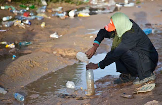 Photo : Refugee from Libya getting water from a puddle