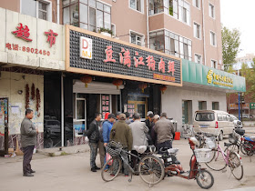 group of men watching and playing a game in front of a dog meat restaurant in Mudanjiang, China