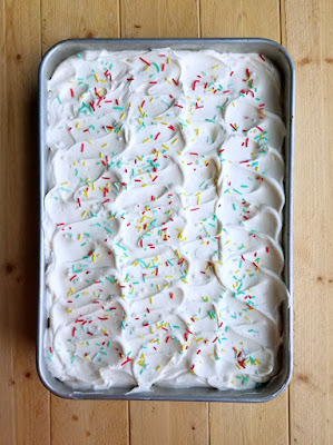 pan of cake topped with swoops of white whipped sweetened condensed milk frosting and sprinkles