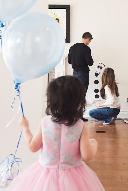 Toddler watches as her parents set up for her party taken during lifestyle family photo session with Melanie Mathieu Photography