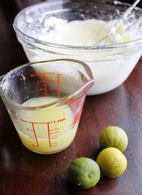 key limes next to measuring cup of key lime juice with bowl of whipped cream cheese in background