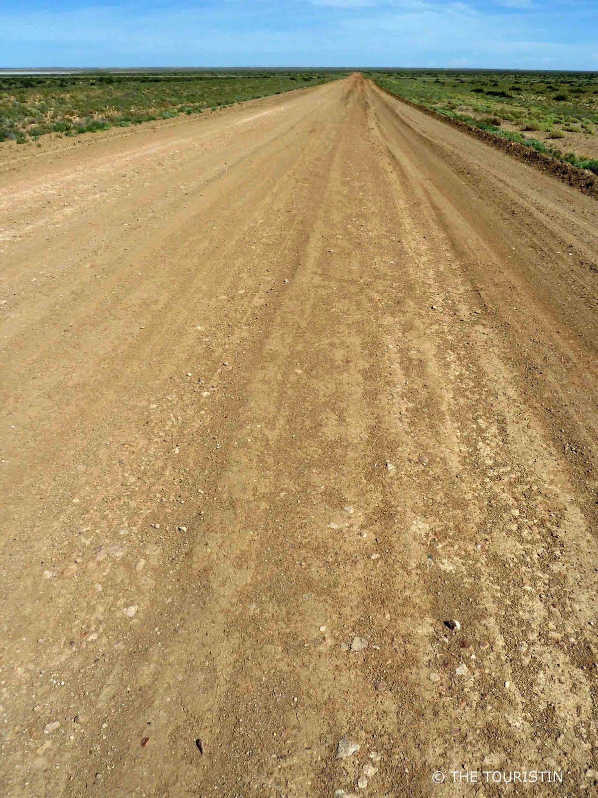A flat dusty untarred road in a seemingly endless flat landscape.