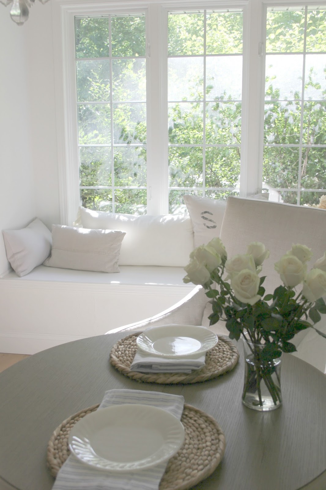 French farmhouse style white kitchen with window seat, linen pillows, slipcovered chairs, and white roses. #frenchcountry #frenchfarmhouse #kitchendecor #serene #whitedecor #farmhousekitchen #hellolovelystudio